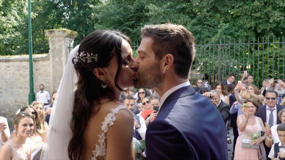 photo de beaux mariés s'embrassant à la sortie de l'église devant les invités poet témoins