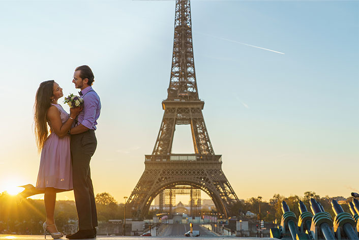 Photographe demande en mariage Paris : séance photo romantique à l'esplanade du Trocadéro au lever du soleil, couple amoureux devant la Tour Eiffel. Fiancée levant le pied avec grâce sous une lumière dorée.