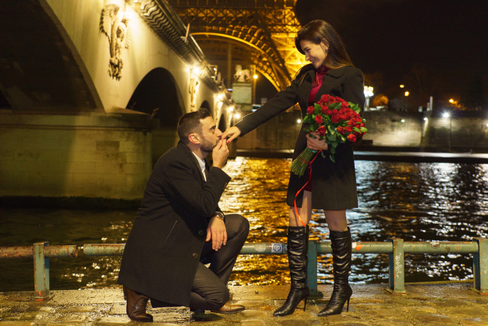 demande en mariage à Paris, homme en genoux avec bouquet de fleurs rouges au port Debilly, Tour Eiffel en arrière-plan la nuit