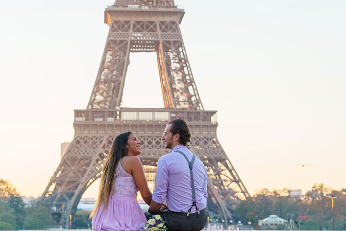 Séance photo demande en mariage Paris : couple assis avec complicité sur l'esplanade du Trocadéro après une demande en mariage romantique au lever du soleil, avec la Tour Eiffel en arrière-plan.
