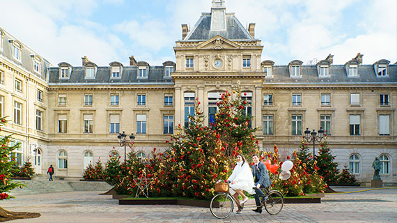 Photo couple mariage originale arrivant à la mairie du 15e de Paris en vélo, avec des ballons attachés à l'arrière. Photographe pour mariage capturant un moment unique du mariage couple à Paris.