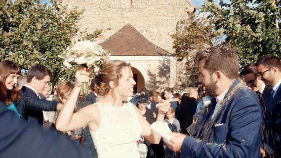 photo de mariée drôle sortant de l'église apres le lancé de fleurs. La belle mariée fait semblant d'engueuler son mari en pointant son doigt vers lui et levant son bouquet comme pour le frapper.